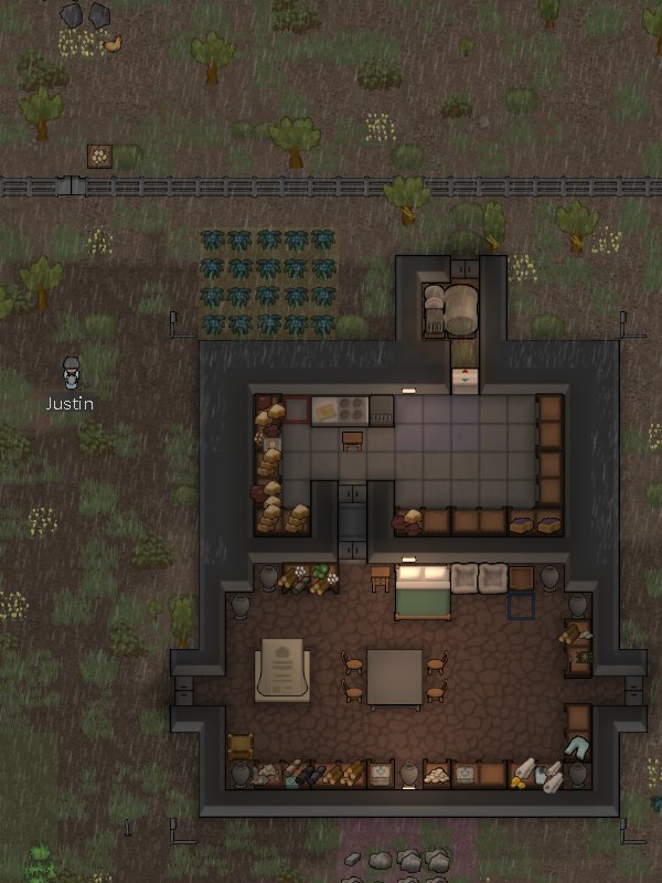 Screenshot of Justin's Rimworld colony: a stone house with a kitchen, storage and a bedroom, a field of crops and his colonist, Justin, outside