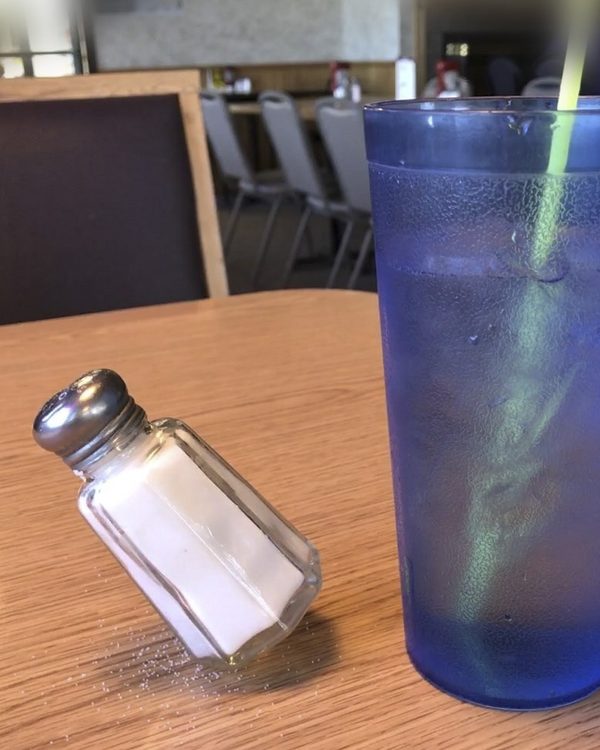 A salt shaker balanced on its side on a restaurant table