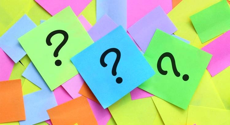 Three sticky notes with question marks on a pile of brightly colored sticky notes