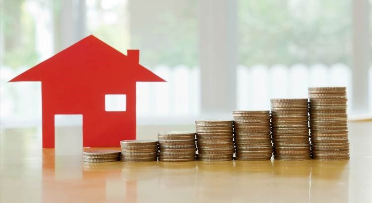 A red paper house beside stacks of coins that get taller from left to right
